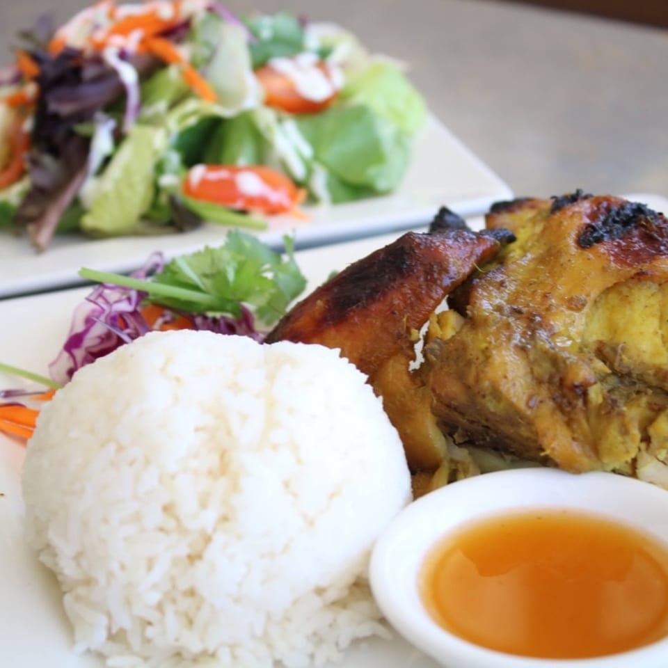 Grilled chicken with rice, a side salad, and dipping sauce on a white plate.