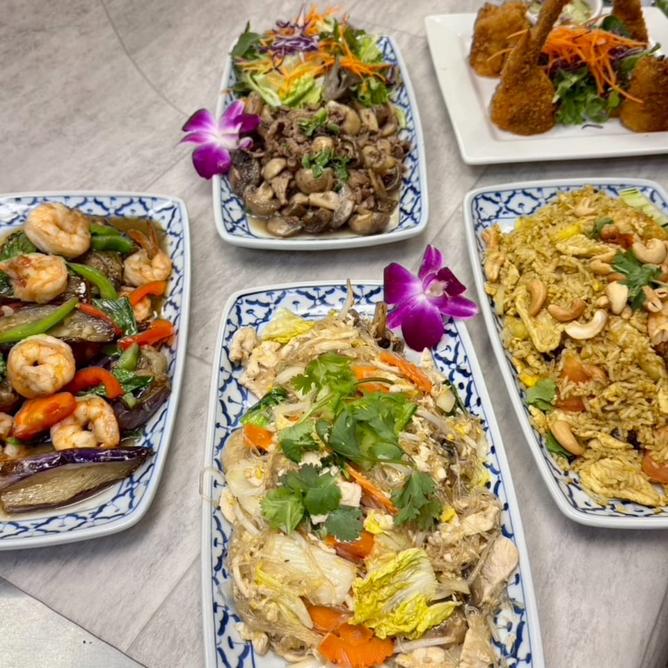 A variety of Thai dishes including fried rice, noodles, shrimp, and mushrooms, garnished with orchids.