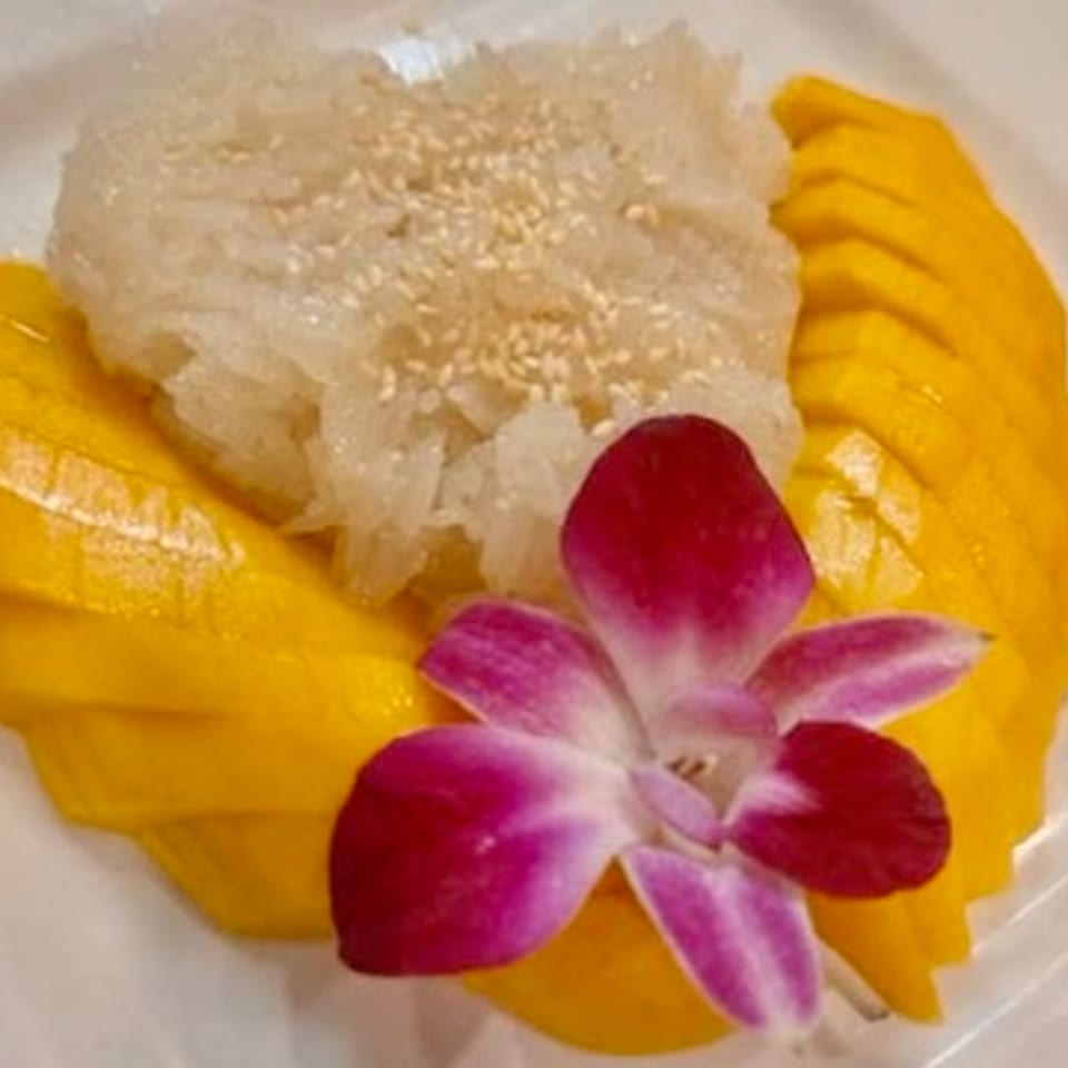 Mango sticky rice with sesame seeds and a purple orchid garnish on a white plate.