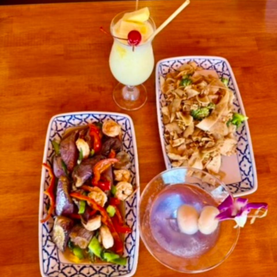 Two Thai dishes, one with noodles and broccoli, the other with vegetables and meat, plus two cocktails.